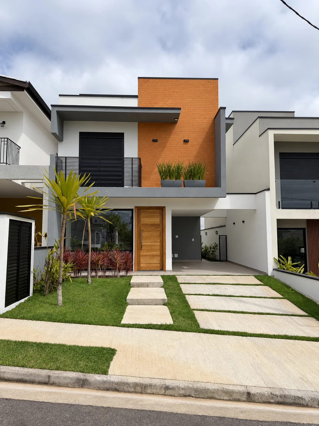 Fachada de dois pavimentos com painel alaranjado, jardim e acesso à garagem